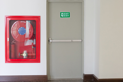 red fire extinguisher on wall next to emergency exit door with green exit sign indicating safety measures in case of fire emergencies